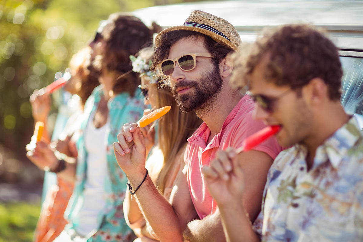 Group of friends wearing sunglasses and eating popsicles outside while enjoying social activities without alcohol
