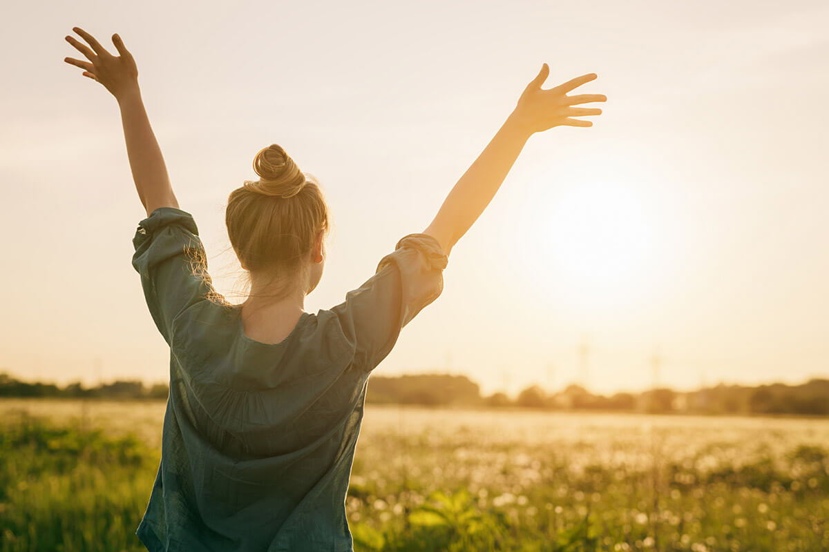 Triumphant person holding up hands to the sky while reaping the benefits of recovering from addiction