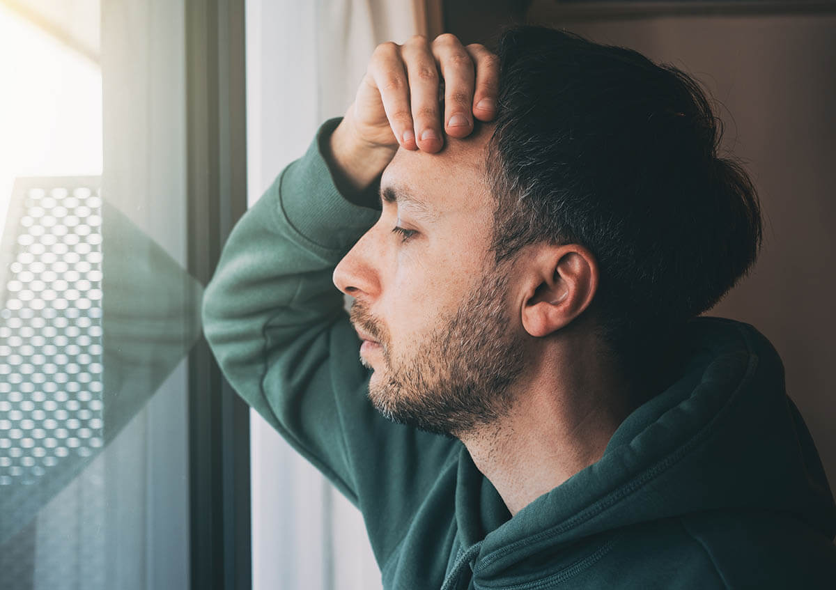 man looking out window and worrying while contemplating answers to the question can alcohol addiction be genetic